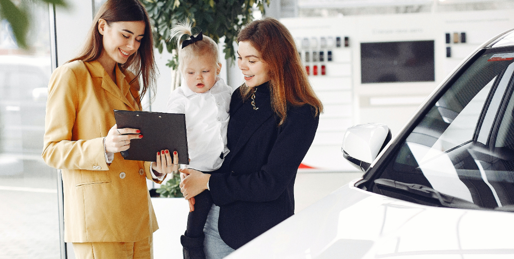 woman holding child and talking to car salesperson