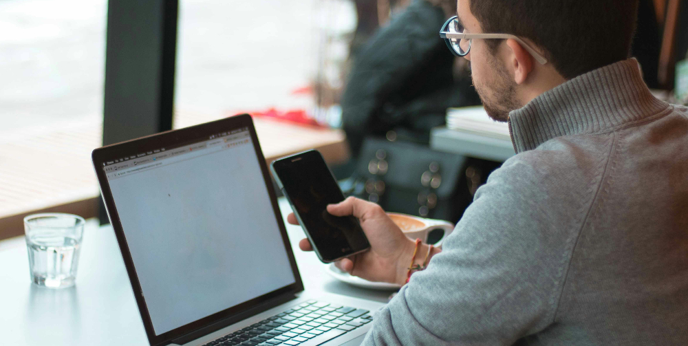 man in grey top on laptop looking at mobile